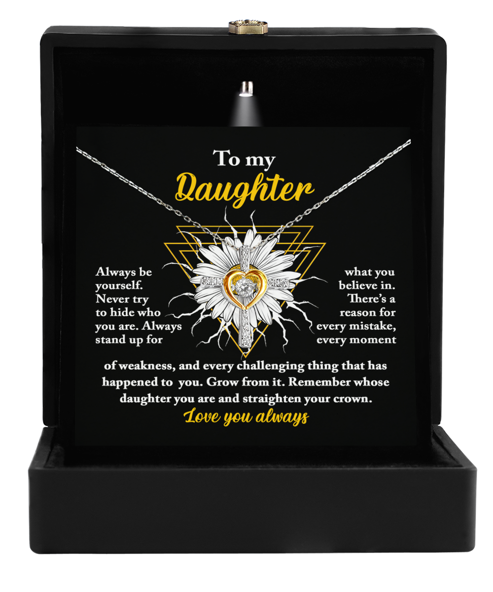 A necklace is displayed in an open black box. The card inside reads, "To my Daughter" and contains a heartfelt message encouraging strength and self-belief. The necklace, named "To Daughter-Be Yourself - Cross Dancing Necklace," features a 14k gold and sterling silver flower pendant with a heart in the center.