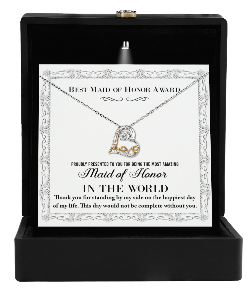 A sterling silver "To Maid of Honor-Of My Life - Love Dancing Necklace" featuring a heart pendant embedded with a small gem is displayed in an open black box. Behind it, a card reads, "Best Maid of Honor Award" and "Maid of Honor in the World," expressing a heartfelt thank-you message for being part of such a special day.