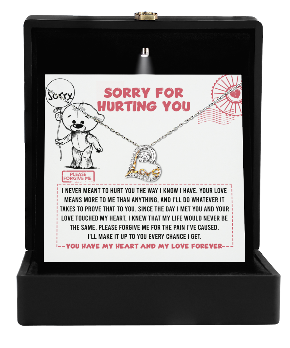 A black box showcases the Sorry-Every Chance - Love Dancing Necklace, a stunning sterling silver piece with a heart pendant. Behind it, a card conveys a heartfelt message reading "Sorry for hurting you," accompanied by an illustrated bear holding a sign that says "Please forgive me.