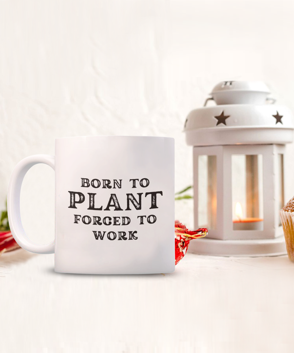 The "Born to Plant Forced to Work" coffee mug, perfect for gardeners, is next to a star-patterned lantern with a candle. This exclusive design is printed and shipped from the USA, not available in stores. Get yours for a limited time!.