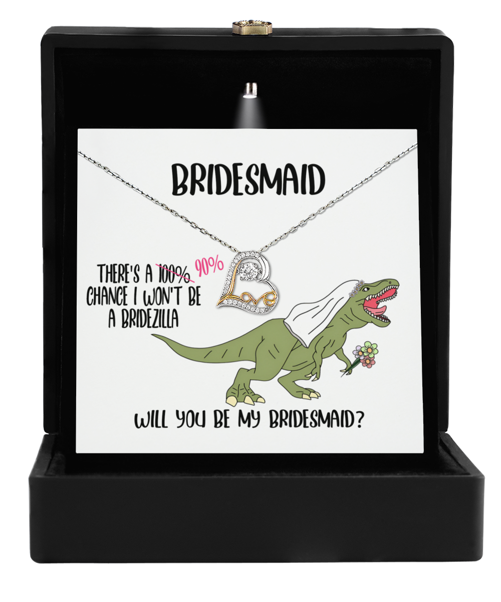 The Bridesmaid-Will You Be - Love Dancing Necklace presents a charming bridesmaid gift box featuring a dinosaur with a veil, a 14k gold pendant, and text humorously stating "There's a 90% chance I won't be a bridezilla. Will you be my bridesmaid?", offering an elegant twist.