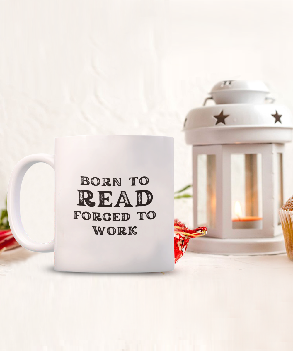 The Born to Read Forced to Work Coffee Mug adds charm beside a lit lantern and cupcake in a cozy setting. Perfect for your reading nook, order this appreciation gift for readers now while supplies last!.