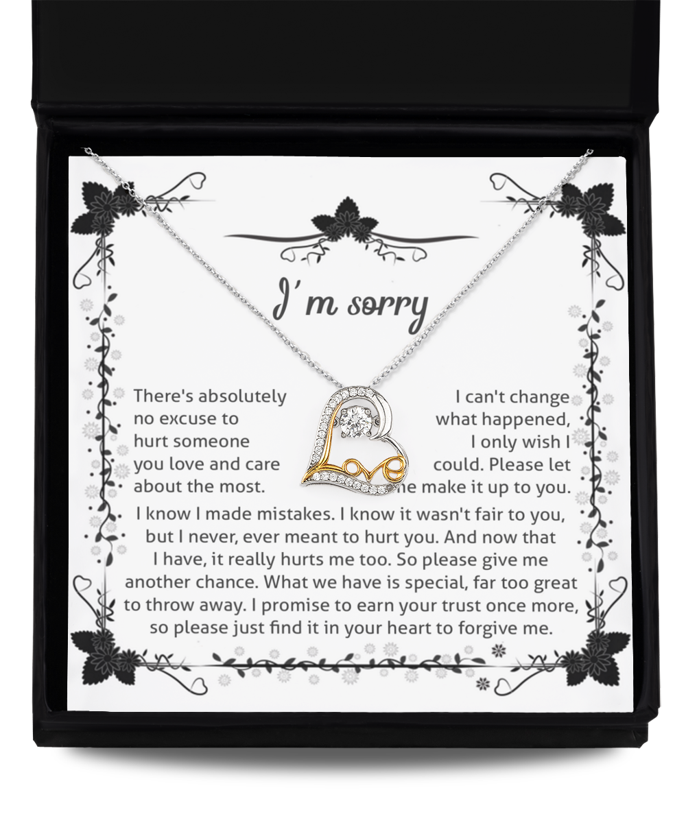 The Sorry-No Excuse - Love Dancing Necklace, a heart-shaped piece crafted from .925 Sterling Silver, lies atop an apology letter inside an open, black gift box. The letter expresses regret, asking for forgiveness and another chance to make things right. Decorative floral borders frame the heartfelt message.