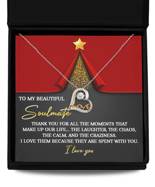 The Soulmate-The Moments - Love Dancing Necklace, crafted in the shape of a heart with two interlocking circles in sterling silver, rests in a jewelry box. A message behind it states, "To my beautiful soulmate... I love you." This elegant necklace perfectly complements the red and gold Christmas tree design.