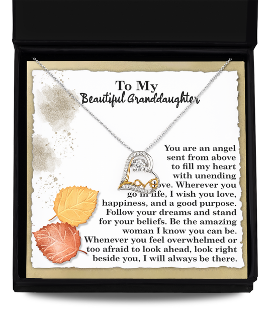 The Granddaughter-An Angel - Love Dancing Necklace, featuring a heart pendant and crafted in 14k gold, rests on a note to a granddaughter with a sentimental message and two autumn leaves.