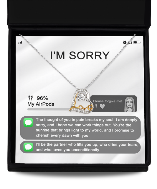 Image of the Sorry-Breaks My Soul - Love Dancing Necklace, a heart-shaped silver and gold piece adorned with gemstones, elegantly placed in a black jewelry box. The background mimics a phone screen displaying an apology text message asking for forgiveness. This sterling silver necklace beautifully captures heartfelt emotions.