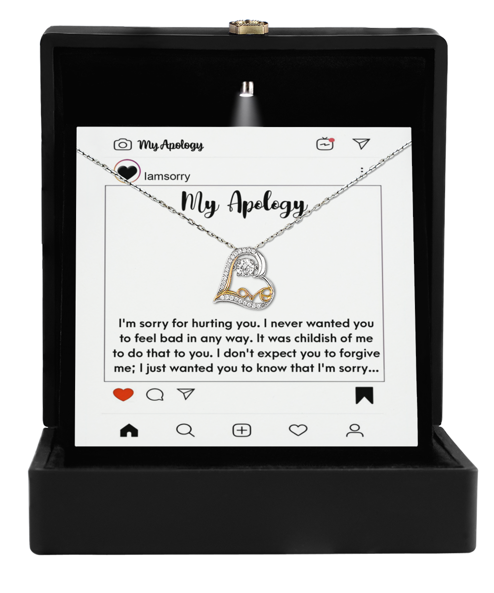 The Sorry-My Apology - Love Dancing Necklace features a 14k gold heart-shaped pendant. It is displayed in a black jewelry box with a printed social media apology message.