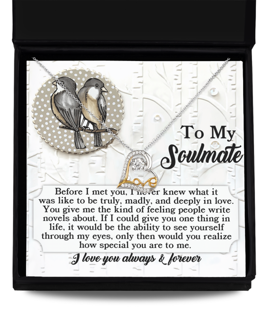 The Soulmate-Write Novels - Love Dancing Necklace features intertwined hearts elegantly displayed on a card adorned with two birds. It is crafted in either elegant Sterling Silver or luxurious 14k Gold and comes with a heartfelt message expressing love for a soulmate.