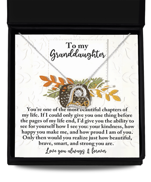 A sterling silver "Granddaughter-How Beautiful - Love Dancing Necklace" is elegantly placed on a card within a box. The card reads: "To my Granddaughter, You're one of the most beautiful chapters of my life..." and is adorned with sparkling cubic zirconia that echoes an affectionate message.