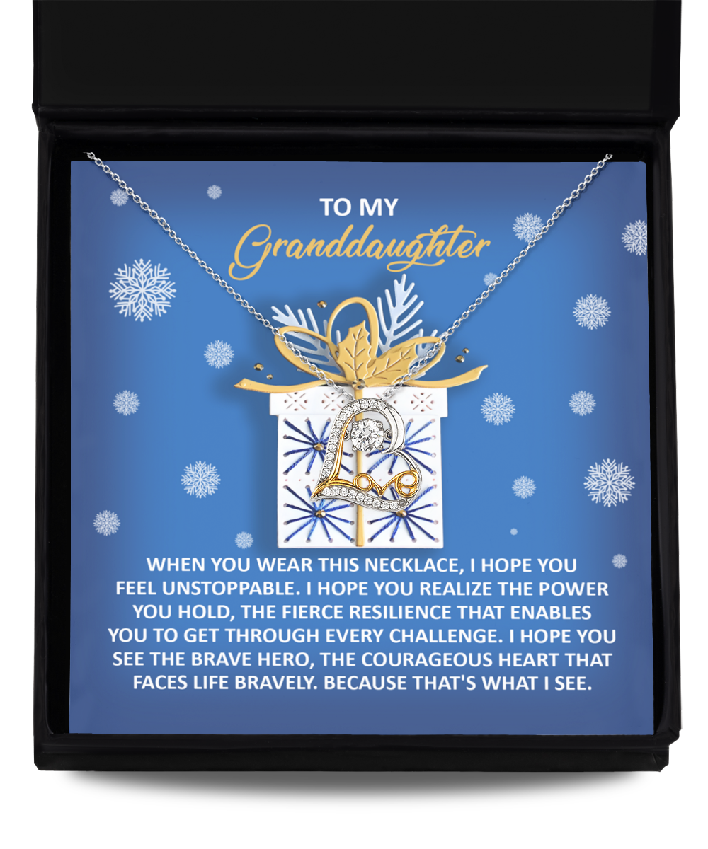 The Granddaughter-Brave Hero Love Dancing Necklace, featuring an elegant pendant, is beautifully showcased in a box containing a heartfelt message for a granddaughter, all set against a blue background. The timeless beauty of this cherished gift is enhanced by its 14k Gold and Sterling Silver blend.