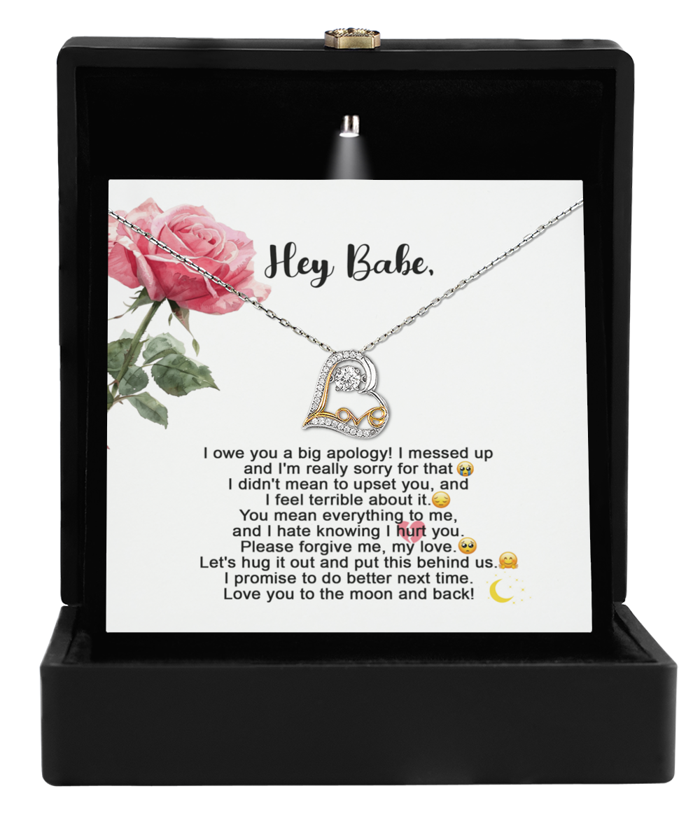 The Sorry-Hug It Out - Love Dancing Necklace, showcasing a stunning heart-shaped pendant crafted in 14k gold, is elegantly displayed in a black box. Alongside this beautiful necklace is a card featuring an apology message complemented by decorative roses, creating the perfect combination of elegance and sentiment.