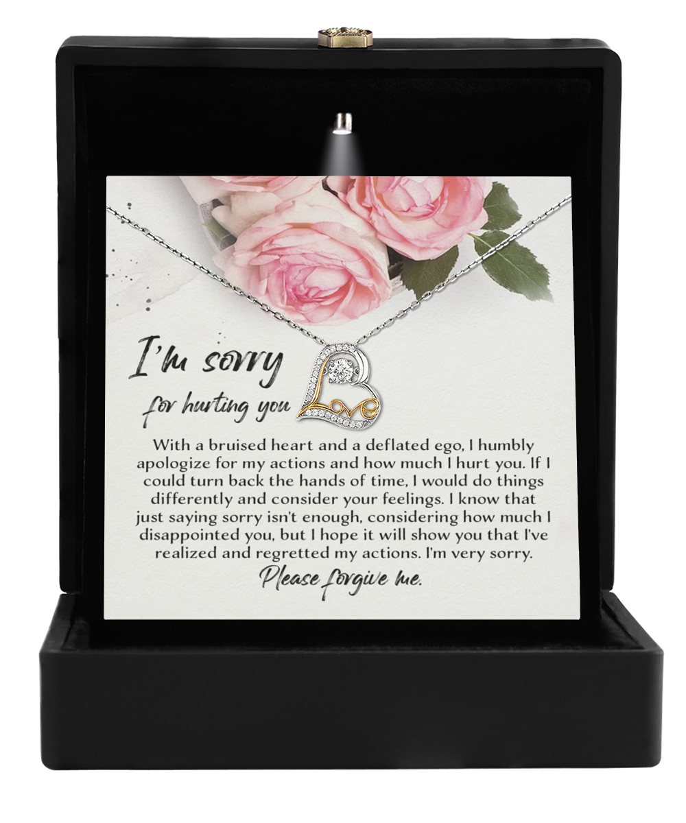 A .925 Sterling Silver heart-shaped pendant from the "Sorry-Regretted My Actions - Love Dancing Necklace" collection, adorned with small cubic zirconia diamonds, is presented in a black box. Alongside the necklace is an apology note with a floral design featuring pink roses, expressing deep regret and seeking forgiveness for causing hurt.