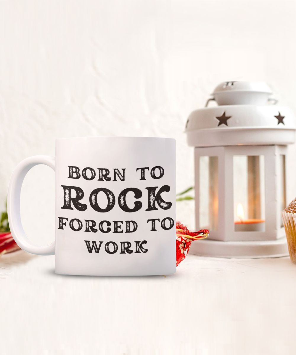 The "Born to Rock Forced to Work" coffee mug, perfect for rockers, is displayed next to a candle lantern and cupcake. Available for a limited time, this USA-printed and shipped item makes for an ideal gift.