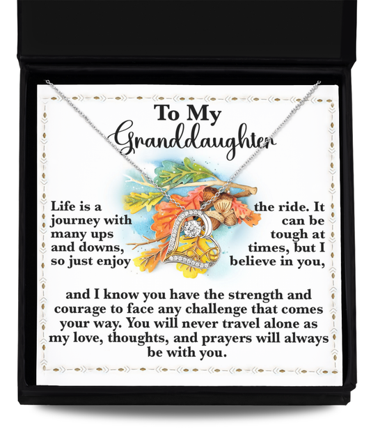 The Granddaughter-Never Travel Alone - Love Dancing Necklace in Sterling Silver is elegantly displayed over a card that reads, "To My Granddaughter," featuring a supportive message about life's journey and the constant assurance of love and prayers.