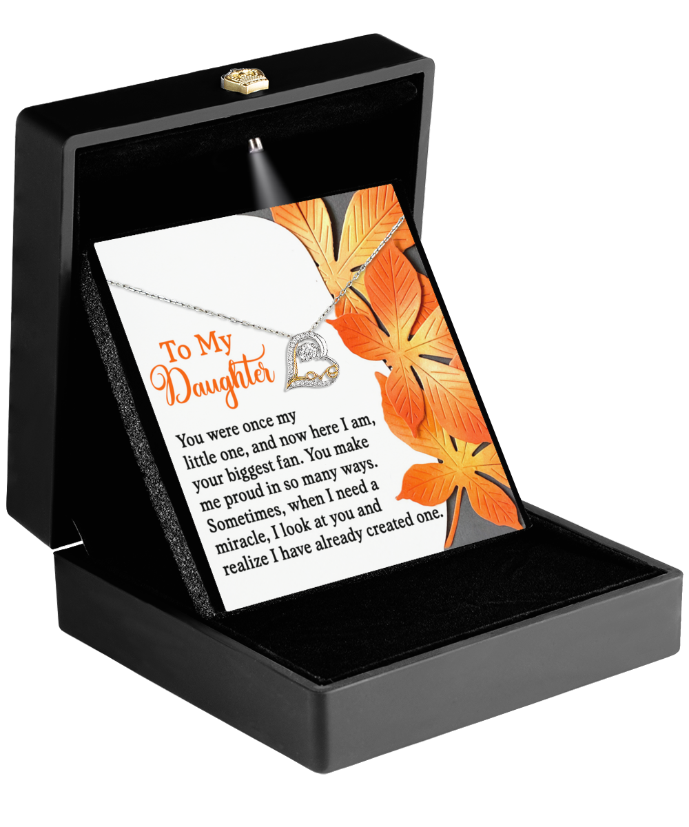 The Daughter-Here I Am - Love Dancing Necklace, featuring a heart-shaped pendant in sterling silver, comes elegantly packaged in a black box. This rhodium-plated piece also includes a card adorned with fall leaves and an inspirational message for your daughter.