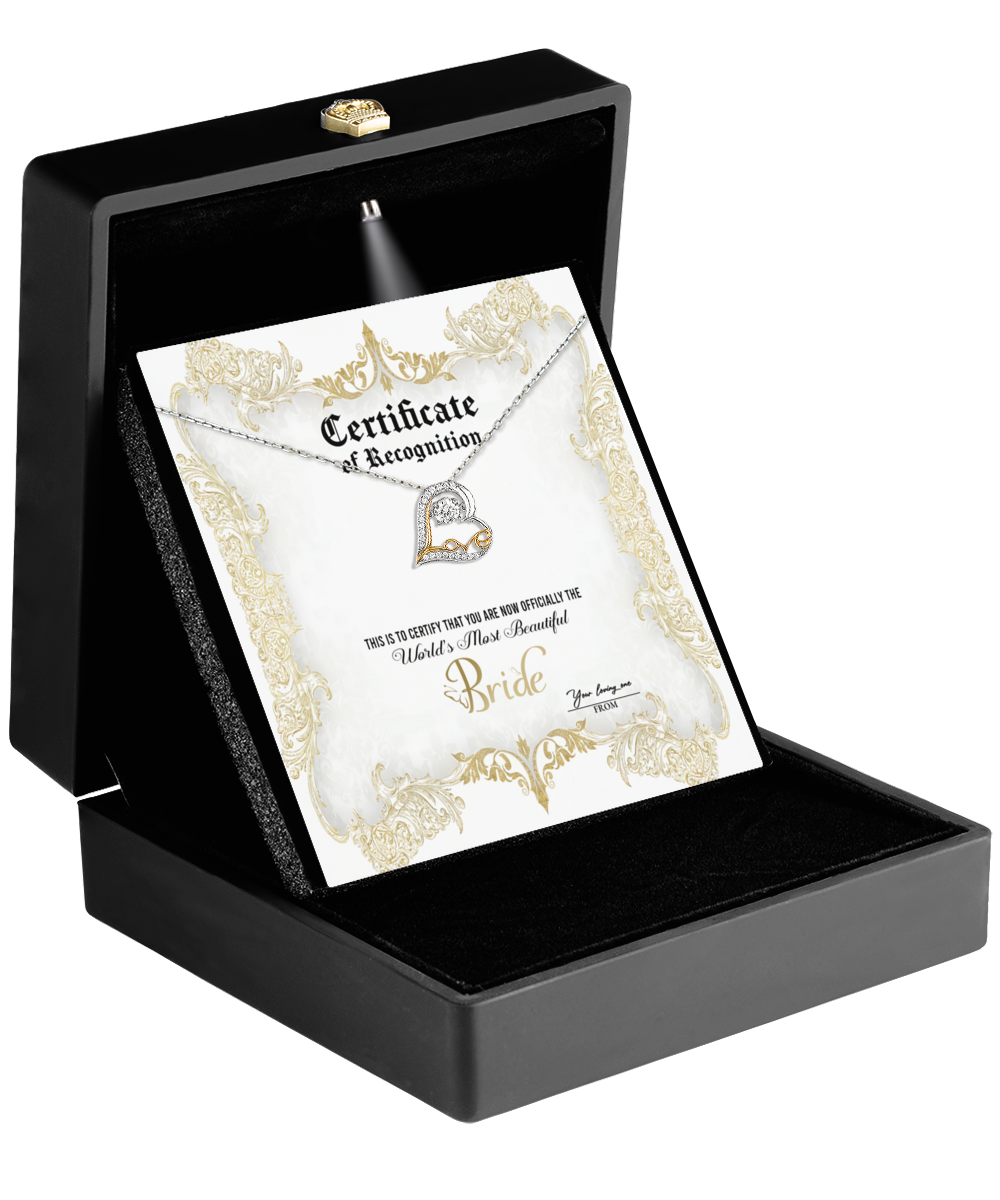 Inside a black box lies the Bride-Certificate Of Achievement - Love Dancing Necklace: a heart-shaped silver necklace featuring two interlocking hearts with a love dancing motif. Complemented by an ornate certificate embellished with gold details, this piece beautifully commemorates enduring romance.