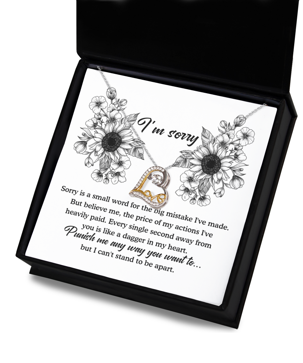 An open black gift box displays the Sorry-Small Word - Love Dancing Necklace, featuring a heart-shaped pendant. The inner card, decorated with a floral design, bears an apology message in both cursive and print fonts that expresses remorse for a mistake and says, "Punish me any way you want to... but I can't stand to be apart.