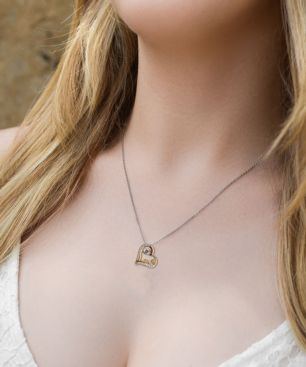 A woman wearing the Bride-Each Moment Together - Love Dancing Necklace, adorned with a heart-shaped pendant and crafted in 14k gold with delicate decorative elements, elegantly draped over a light-colored top. This necklace makes for a perfect thoughtful gift for a bride.