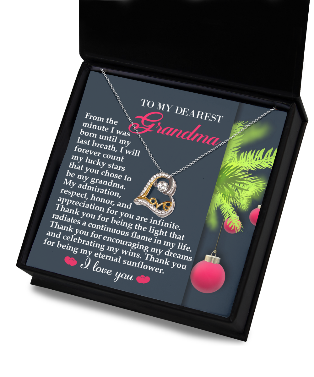 The Grandma-Eternal Sunflower - Love Dancing Necklace, featuring a heart pendant and heartfelt message, expresses maternal love and gratitude. It arrives in a box adorned with holiday-themed decorations.