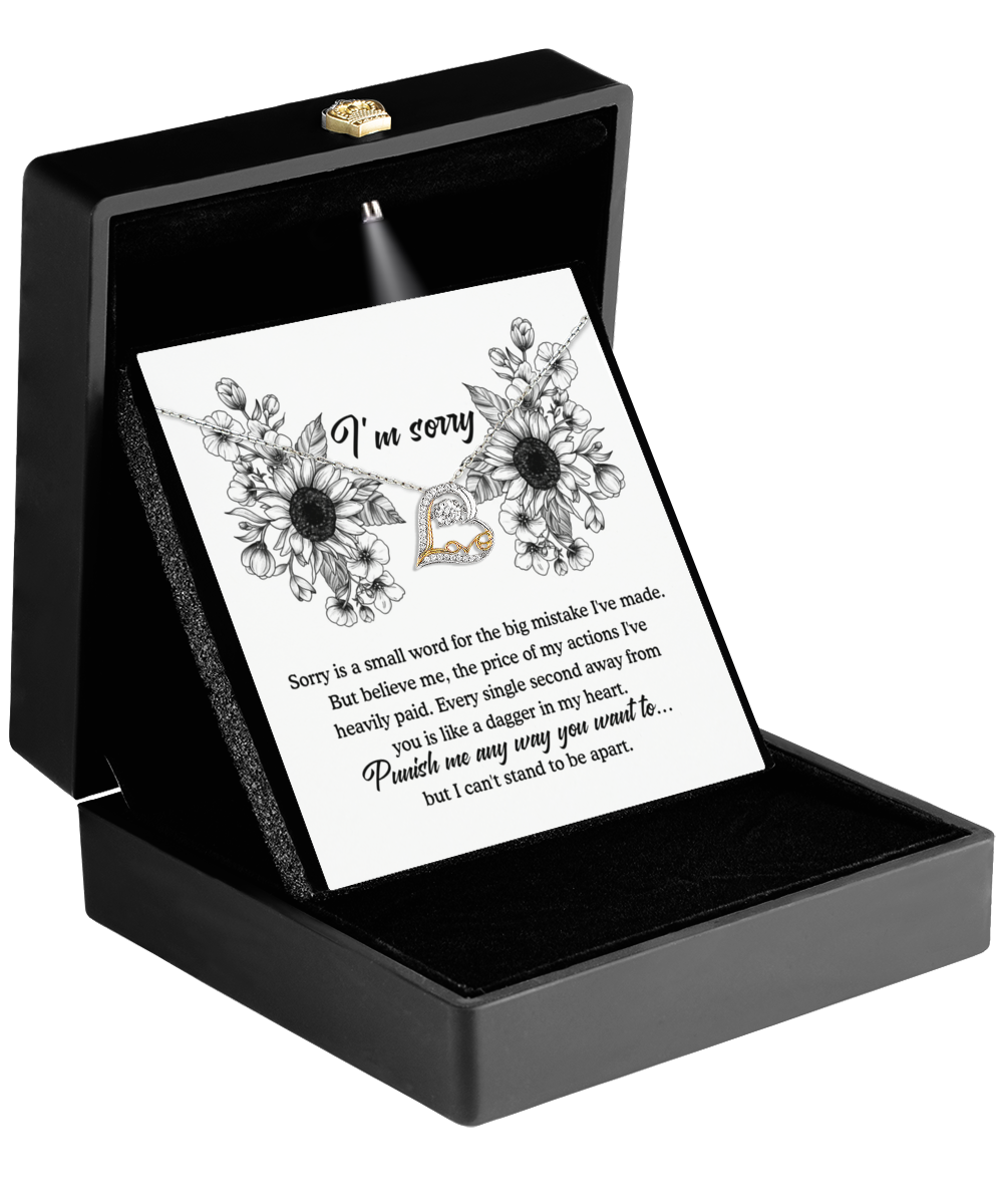 A black jewelry box showcasing the Sorry-Small Word - Love Dancing Necklace, featuring a sterling silver heart pendant. The lid illuminates a card inside with a spotlight, which begins with the apology message "I'm sorry" and delves deeper into its importance. The card is embellished with floral illustrations, lending an elegant touch.