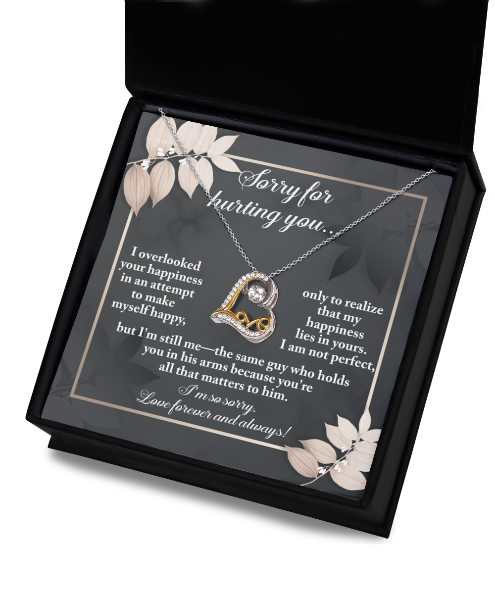 A heartfelt note within a black box accompanies the Sorry-Lies In Yours - Love Dancing Necklace, featuring a 14k gold loop enclosing a heart and a message apologizing for hurting the recipient while expressing enduring love and regret.