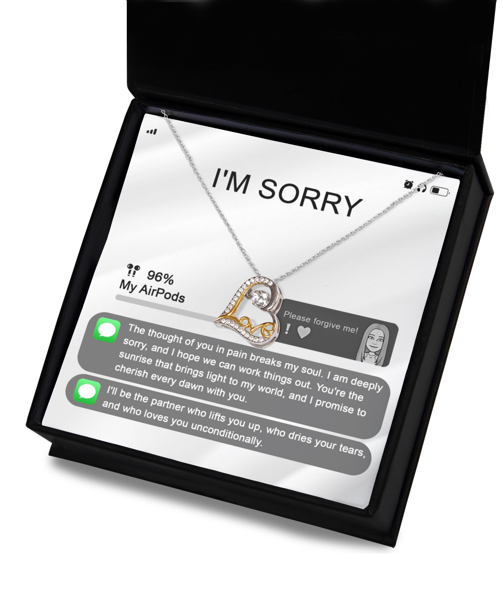 Image of the Sorry-Breaks My Soul - Love Dancing Necklace, a heart-shaped silver and gold piece adorned with gemstones, elegantly placed in a black jewelry box. The background mimics a phone screen displaying an apology text message asking for forgiveness. This sterling silver necklace beautifully captures heartfelt emotions.