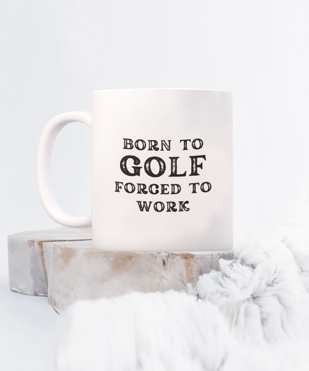 The "Born to Golf Forced to Work" coffee mug, perfect for golf enthusiasts, features text on white ceramic and sits on a wooden surface with soft fabric. Printed and shipped from the USA, it ensures a safe checkout and is available for a limited time.