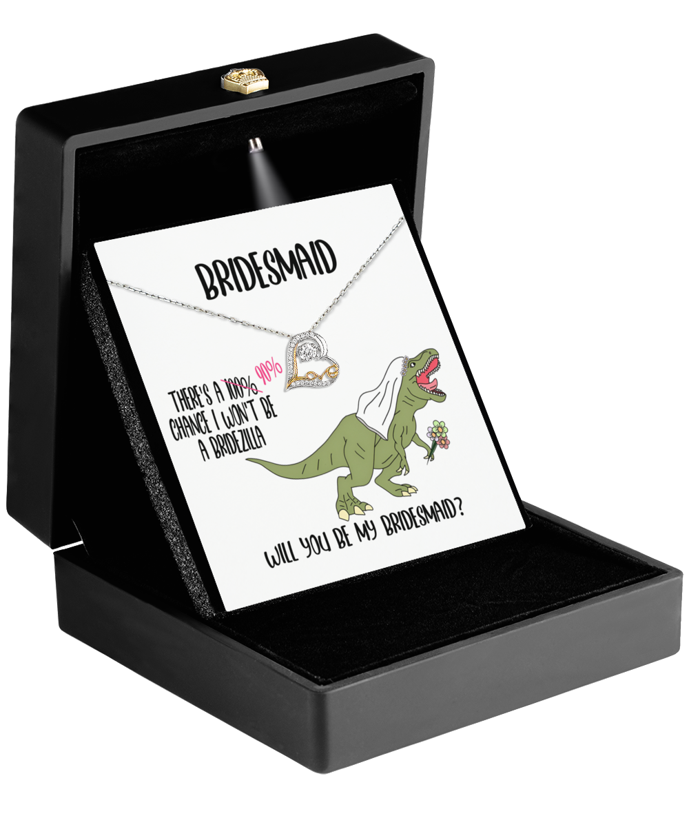 The open black jewelry box showcases the Bridesmaid-Will You Be - Love Dancing Necklace, complete with a heart pendant, making it an ideal gift for a bridesmaid. The accompanying card reads "Bridesmaid" and includes a whimsical illustration of a dinosaur wearing a veil and holding flowers, enhancing the charm of this 14k gold piece.