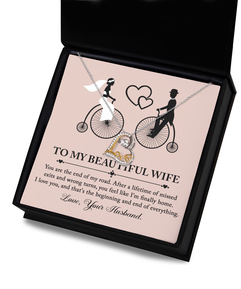 A beautiful To Wife, I'm Finally Home - Love Dancing Necklace in a box adorned with an illustration of a bride and groom on bicycles. The box, featuring the message "To My Beautiful Wife," expresses love and appreciation from "Your Husband." This necklace is crafted with .925 Sterling Silver, making it a timeless keepsake.