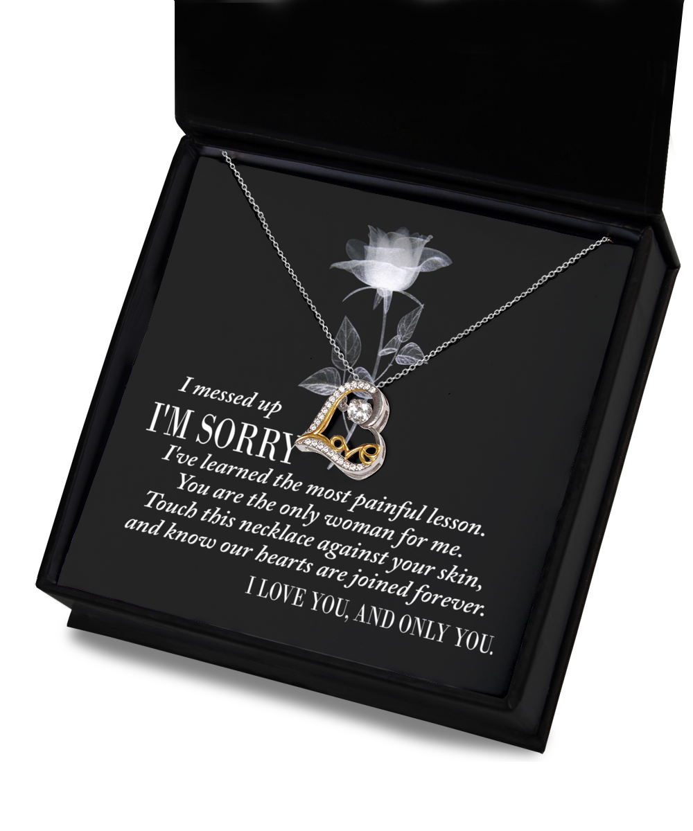 Sorry-Painful Lesson - Love Dancing Necklace: A silver, heart-shaped necklace adorned with a gold accent and a diamond, presented in a black box. The box liner features an apology message and a statement of love. Expertly crafted with genuine .925 sterling silver, it showcases the enduring beauty of AAAAA Cubic Zirconia.