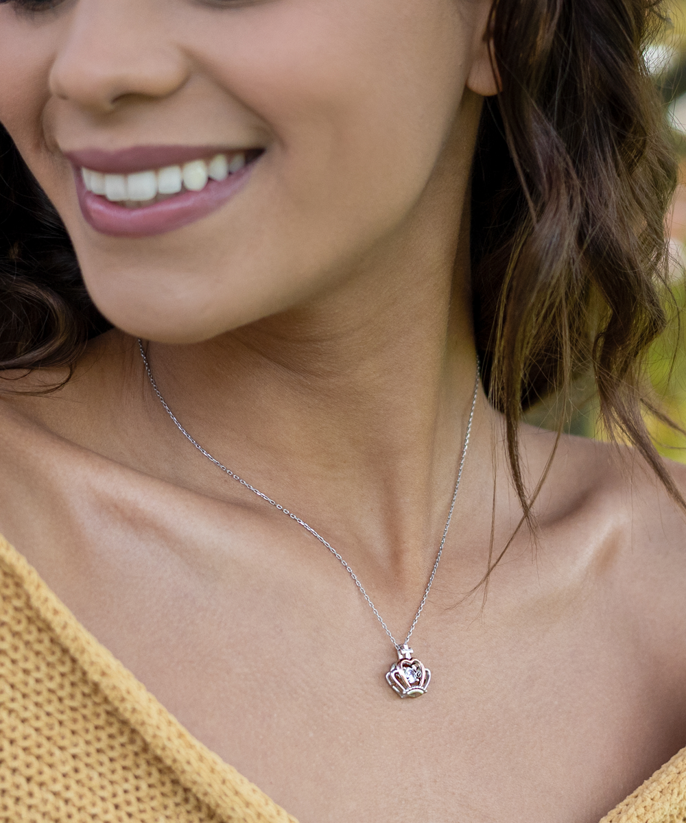 A close-up of a smiling woman wearing a delicate necklace with a heart-shaped pendant, perfect as a "To Boyfriend's Mom, As Your Own" - Crown Pendant Necklace from Gearbubble.