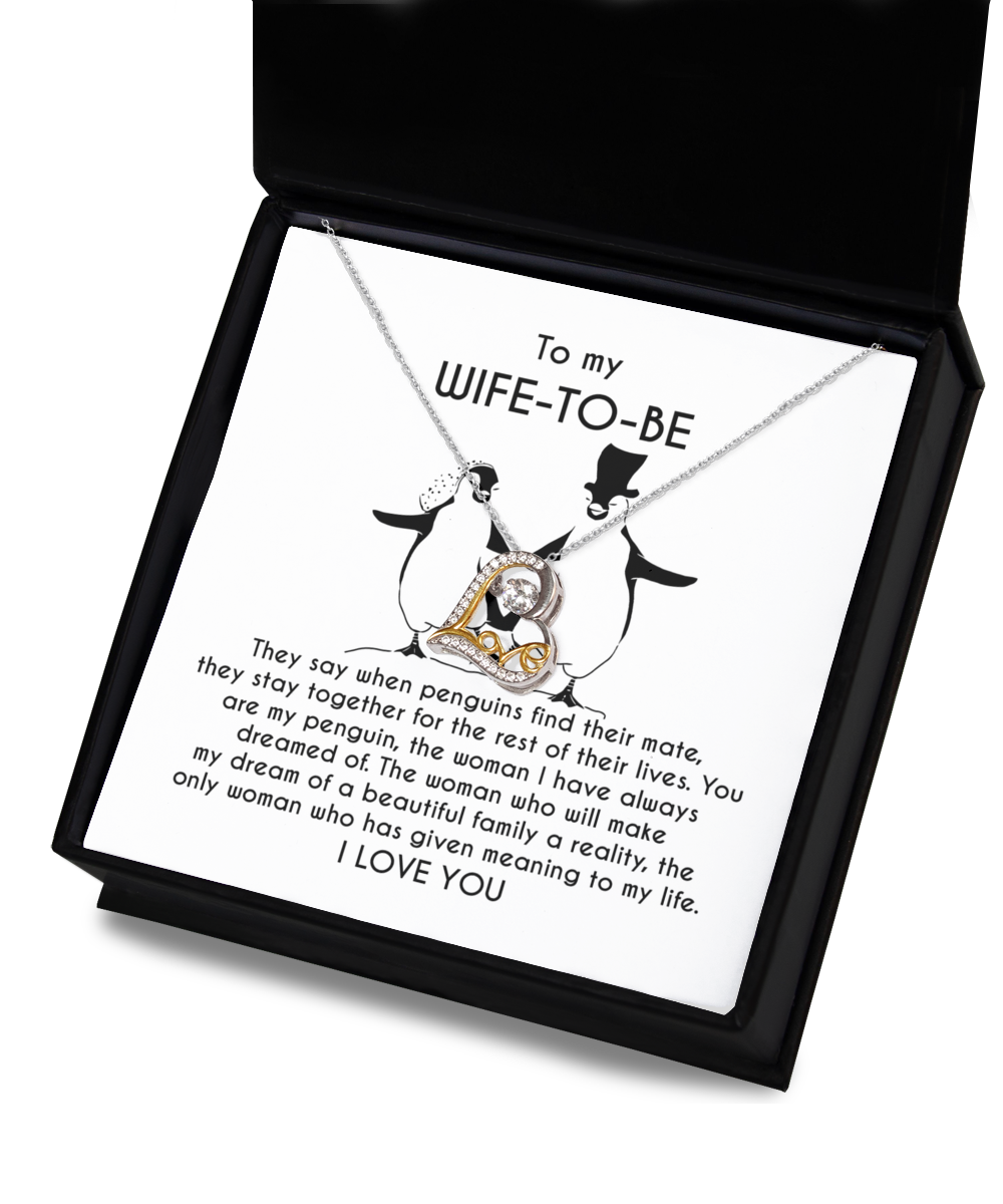 A silver heart-shaped necklace with an intertwined 14k gold plated heart centerpiece sits on a message card inside a black box. The card reads: "To my WIFE-TO-BE, I LOVE YOU" with a monologue about love and penguins. This is the Wife-to-be-My Penguin - Love Dancing Necklace.