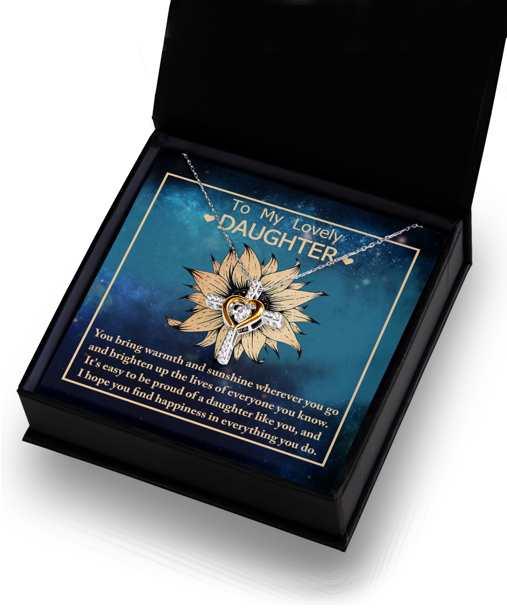 Inside an open black gift box, a rhodium-plated, silver necklace with a cross-shaped pendant gleams. The box also contains a card with an illustration of a sunflower against a blue background and a heartfelt message that reads, "To My Lovely Daughter-Be Proud Of" followed by an uplifting note.