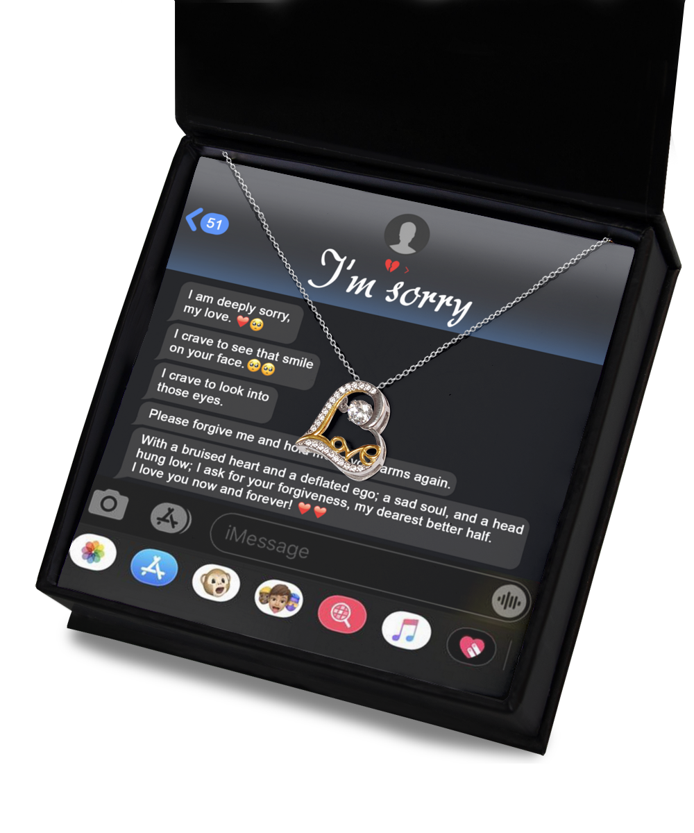 A Sorry-Rebuild Our Connection - Love Dancing Necklace, featuring a heart-shaped pendant crafted from silver and 14k gold, is placed inside a jewelry box. The background displays a message on a phone screen saying "I'm sorry" and a heartfelt apology.