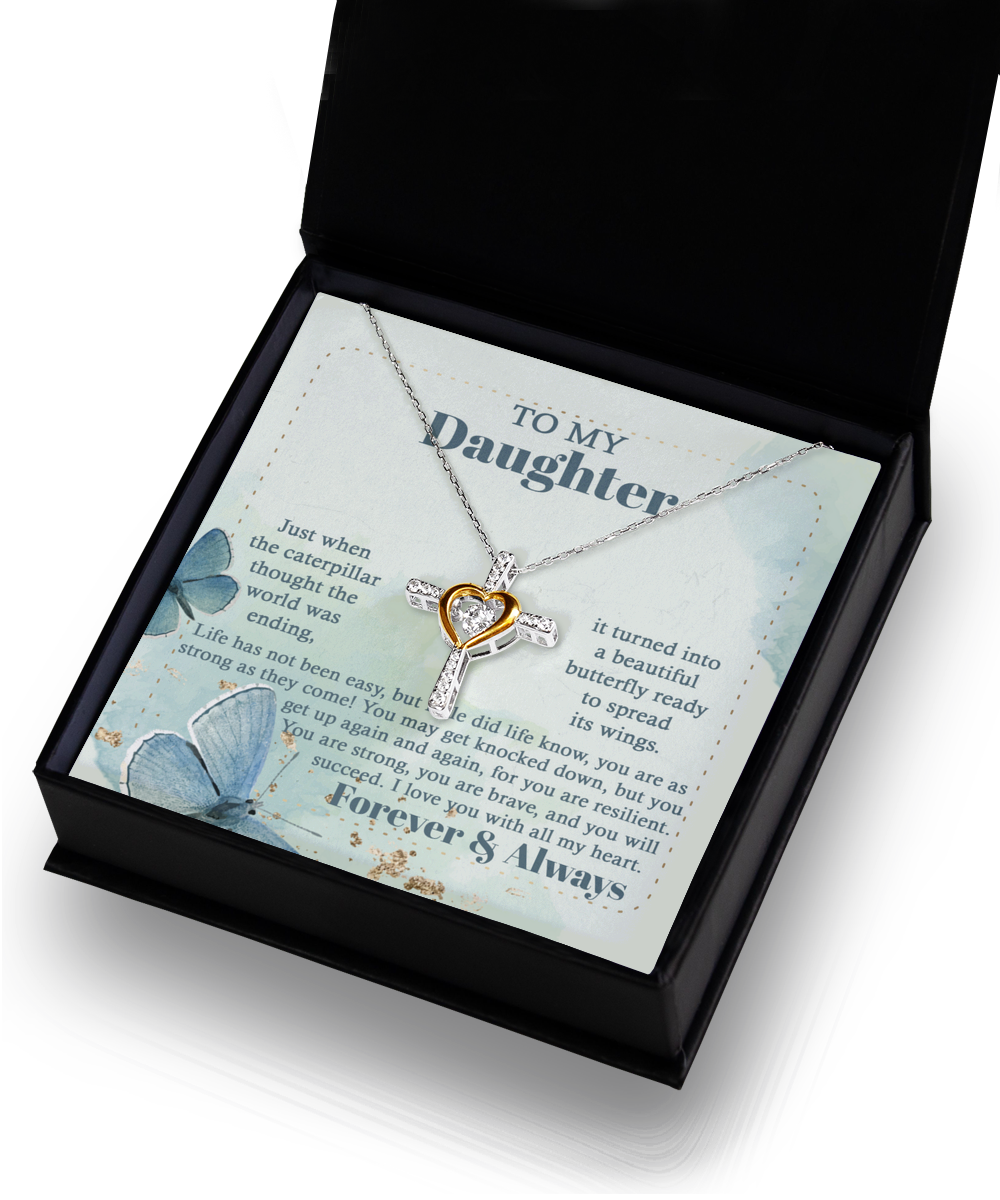 A gift box containing the "To Daughter-Beautiful Butterfly - Cross Dancing Necklace," featuring a sterling silver cross with a 14k gold heart at the center. The box also includes a heartfelt message printed on blue cardstock with butterfly designs, addressed "To My Daughter," expressing love and encouragement.