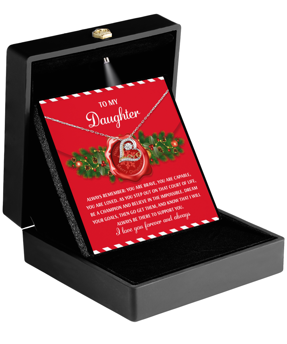 A "Daughter-Be A Champion - Love Dancing Necklace" with a heart-shaped pendant and a red card rests in an open black box. The card bears a heartfelt message surrounded by holly, making it an ideal gift.