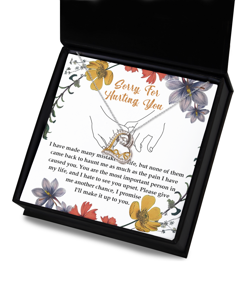 A stunning Sorry-Haunt Me - Love Dancing Necklace featuring an intertwined heart pendant, crafted in sterling silver, rests on a card that reads, "Sorry for hurting you," along with an apology message below. The card is beautifully decorated with floral illustrations.