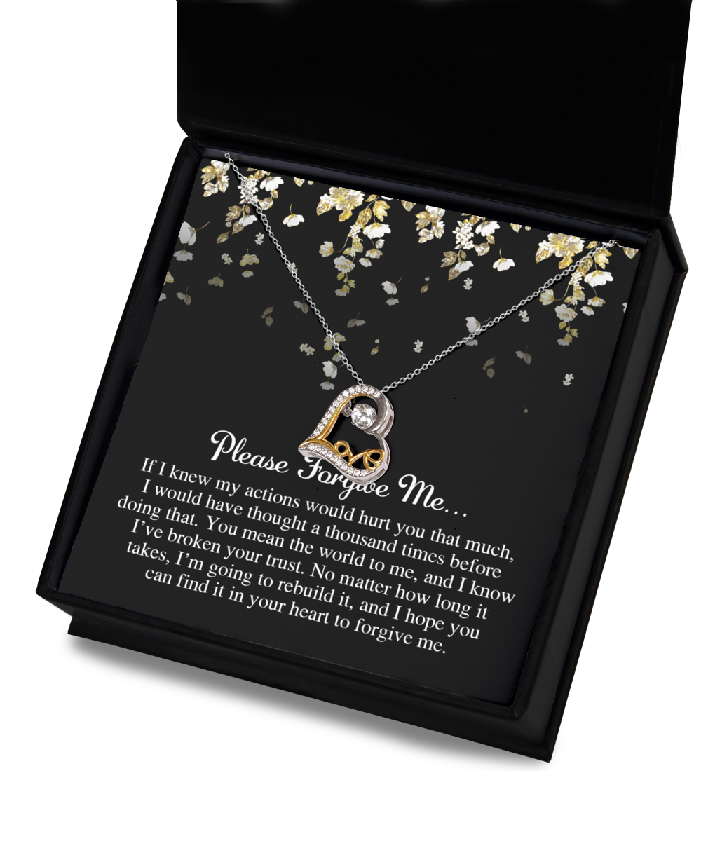 The "Sorry-Broken Your Trust - Love Dancing Necklace" features a heart-shaped pendant with a central gem, beautifully displayed in an open black box. The background of the box is adorned with floral designs and text expressing an apology. This enchanting necklace is available in sterling silver or 14k gold, adding a touch of elegance.