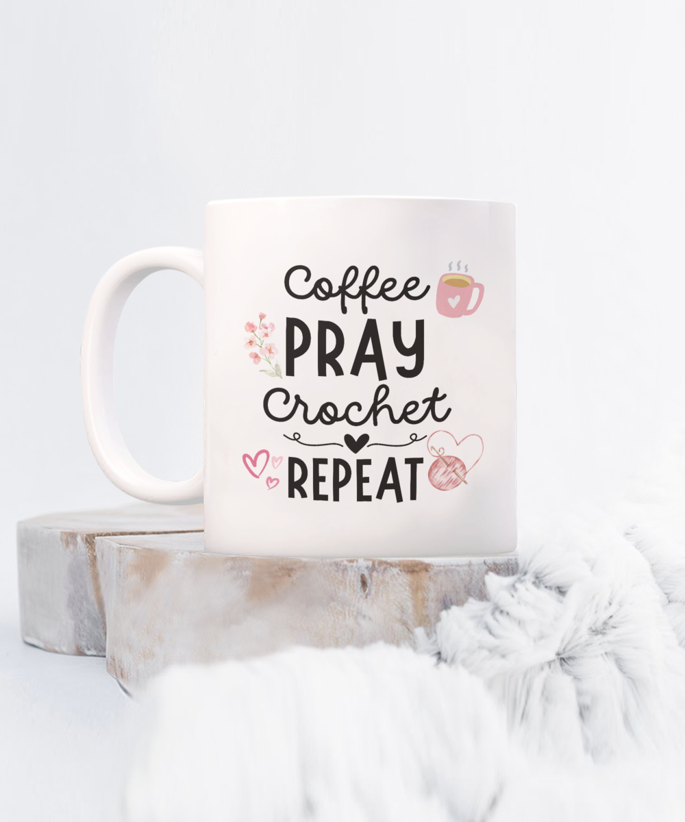 The "Coffee Pray Crochet Repeat" mug, featuring heart and coffee cup illustrations, is set on a fuzzy surface and wooden platform. Shipped from the USA, this mug is available for a limited time only and not in stores.