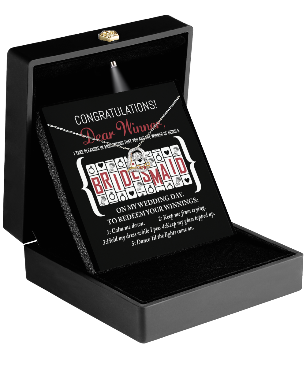 A black box from the "To Bridesmaid - The Winner Of - Love Dancing Necklace" collection contains a card with a sterling silver necklace. The card reads, "Congratulations Dear Winner!" and features a row of slot machine images revealing the word "Bridesmaid." Below, there are instructions for redeeming winnings on the wedding day, such as calming the bride and keeping the wine topped up.