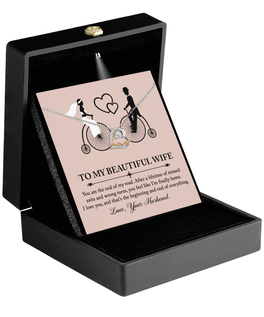 The "To Wife, I'm Finally Home - Love Dancing Necklace" makes the perfect gift for your wife with its gold heart-shaped pendant featuring a couple on bikes design, beautifully presented in a black box with a heartfelt message inside.