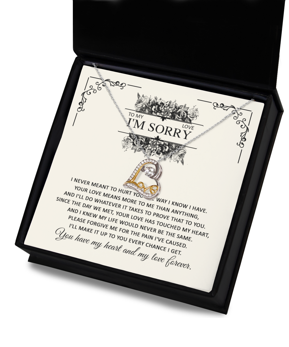 An open black gift box featuring the Sorry-Every Chance - Love Dancing Necklace, which showcases a pendant spelling "LOVE" in sterling silver hypoallergenic and 14k gold, adorned with a sparkling gem. Behind the necklace is a heartfelt apology note printed on white paper, expressing regret and seeking forgiveness.