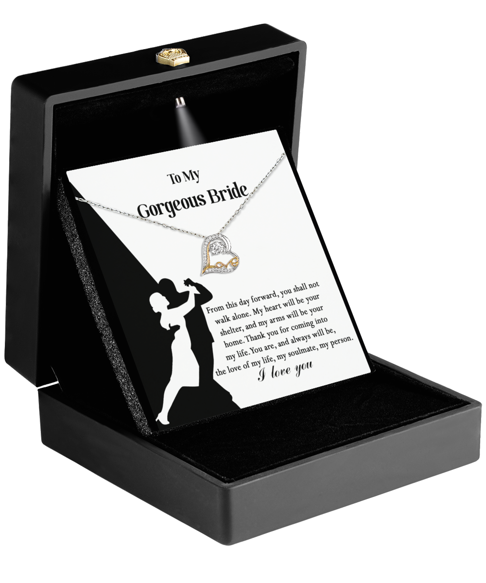 A heart-shaped gold pendant rests elegantly in an open black box, accompanied by a card that reads "To My Gorgeous Bride" and showcases a silhouetted couple. The Bride-Be Your Home - Love Dancing Necklace perfectly embodies the essence of love and devotion, making it an exceptional bridal gift.