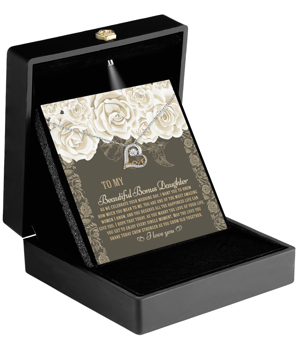 Open a black box showcasing the "To Bonus Daughter-Grow Old Together - Love Dancing Necklace" nestled beside a card adorned with white roses and a heartfelt message, making it the perfect wedding gift for a bonus daughter.