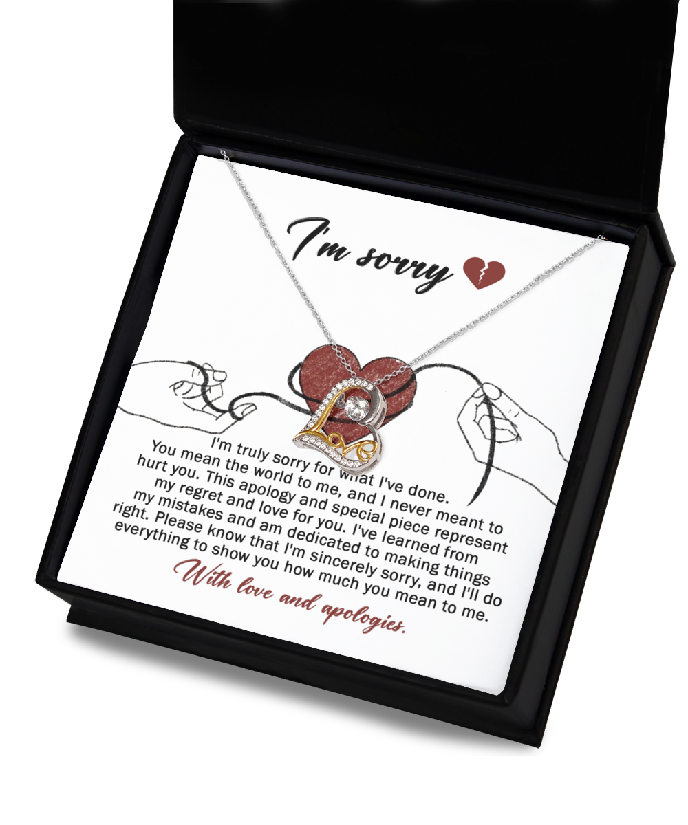 The "Sorry-Mean The World - Love Dancing Necklace," featuring a heart pendant, is displayed in a black box. The interior of the box is lined with 14k gold and includes an apology message expressing regret and love, along with an illustration of two hands holding red string.