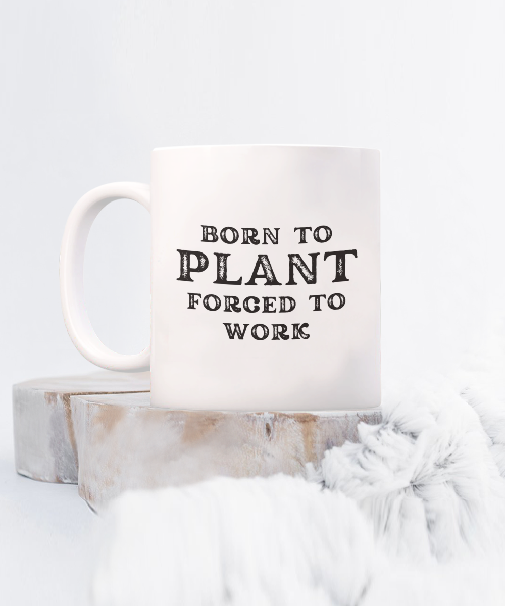 A "Born to Plant Forced to Work" white mug sits on wood coasters, paired with a cozy blanket. Printed and shipped from the USA, it's NOT store-available. Grab this unique gardener gift for a limited time!.