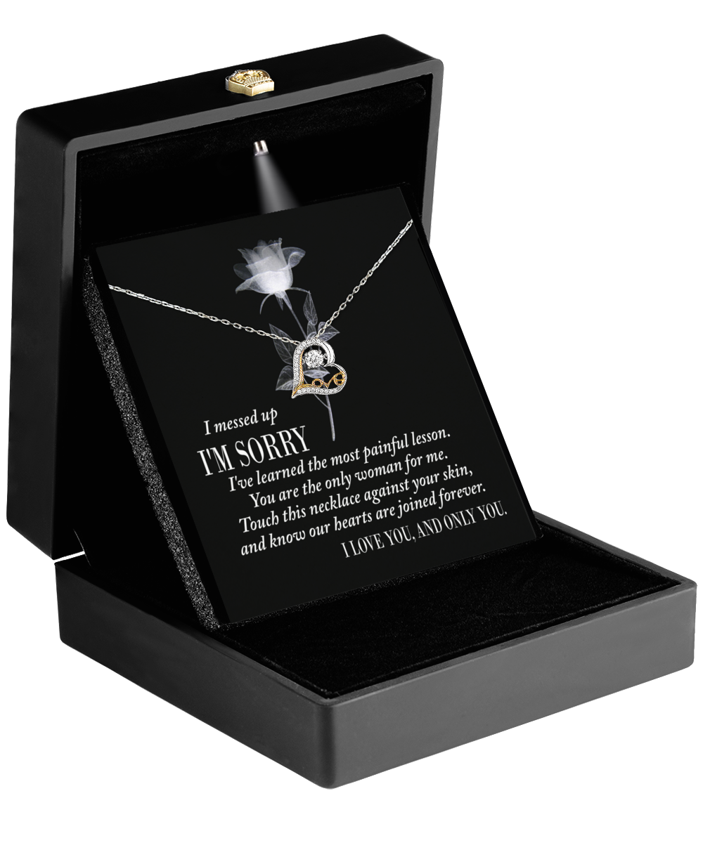 The "Sorry-Painful Lesson - Love Dancing Necklace" features interlocking hearts in 14k gold with a diamond, elegantly displayed in a black box. It includes an apology note expressing deep love and regret.