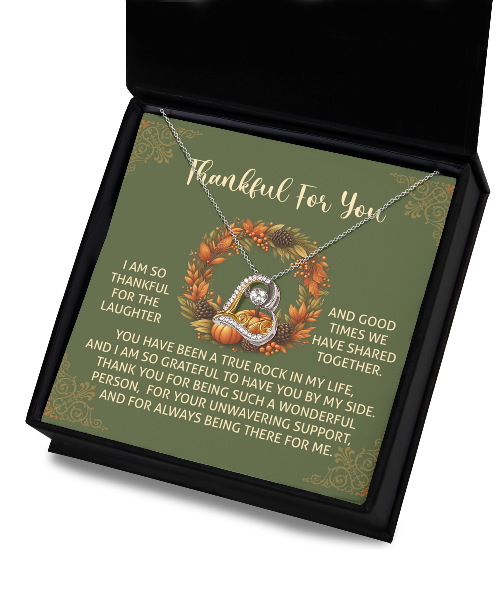 The Thanksgiving-By My Side - Love Dancing Necklace, featuring a circular pendant that sparkles in 14k gold, is beautifully presented in an open box. Behind it, a card with a Thanksgiving message is accompanied by autumn leaves and pumpkins, setting a festive and cozy scene.