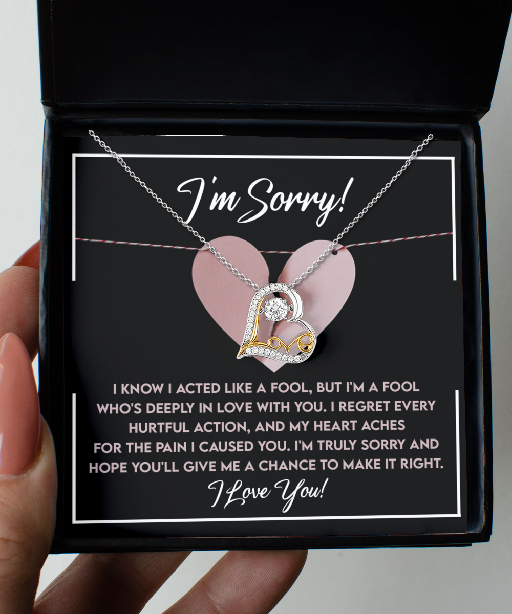 A hand holding an open box with a Sorry-Deeply In Love - Love Dancing Necklace, crafted in genuine .925 Sterling Silver. The inside of the box has a message of apology stating, "I'm Sorry!" followed by a heartfelt note about regret and asking for a chance to make it right.