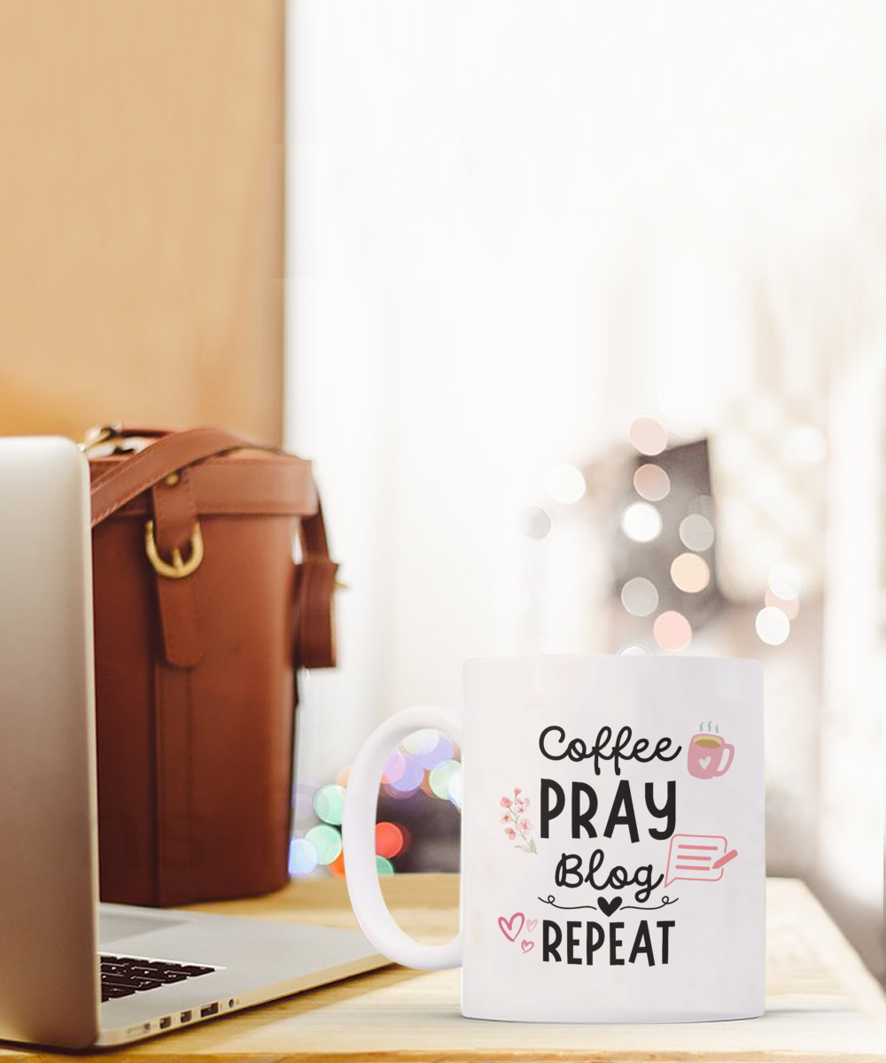 The "Coffee Pray Blog Repeat" coffee mug, perfect for bloggers, sits next to a laptop and brown bag. Printed and shipped from the USA, this limited-time item ensures you're stylish while working or relaxing.